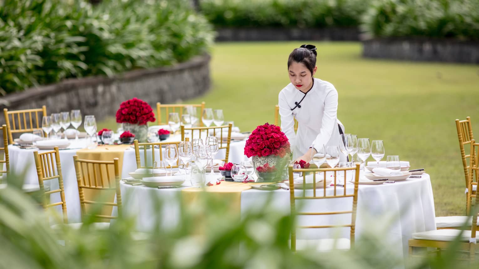 A staff member sets a table out in the lawn with red flowers for a wedding