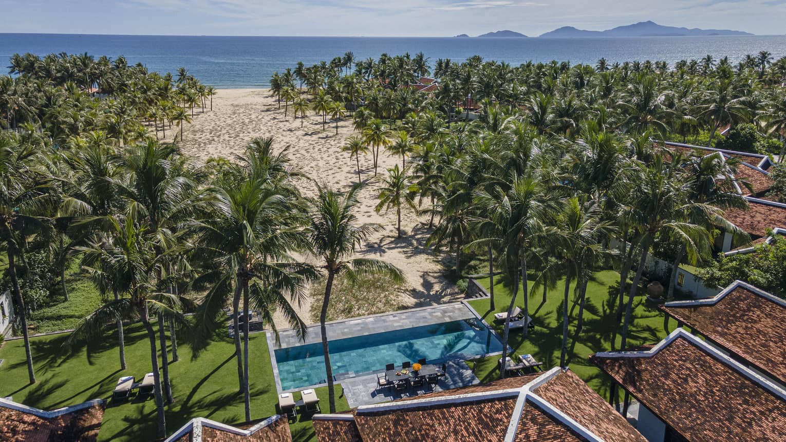 Four Bedroom Pool Villa aerial shot with ocean and mountain views, palm trees and blue skies