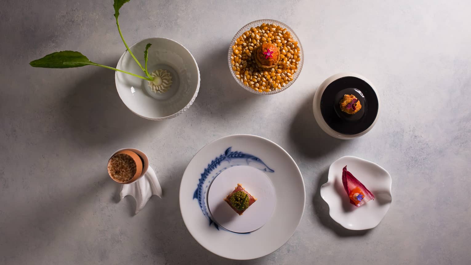 Overhead view of six small bowls of amuse bouches on a white marble table