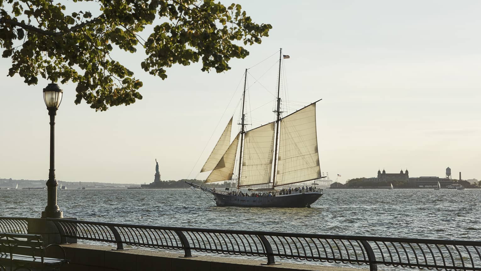 View from boardwalk as sailboat glides past Statue of Liberty in river 