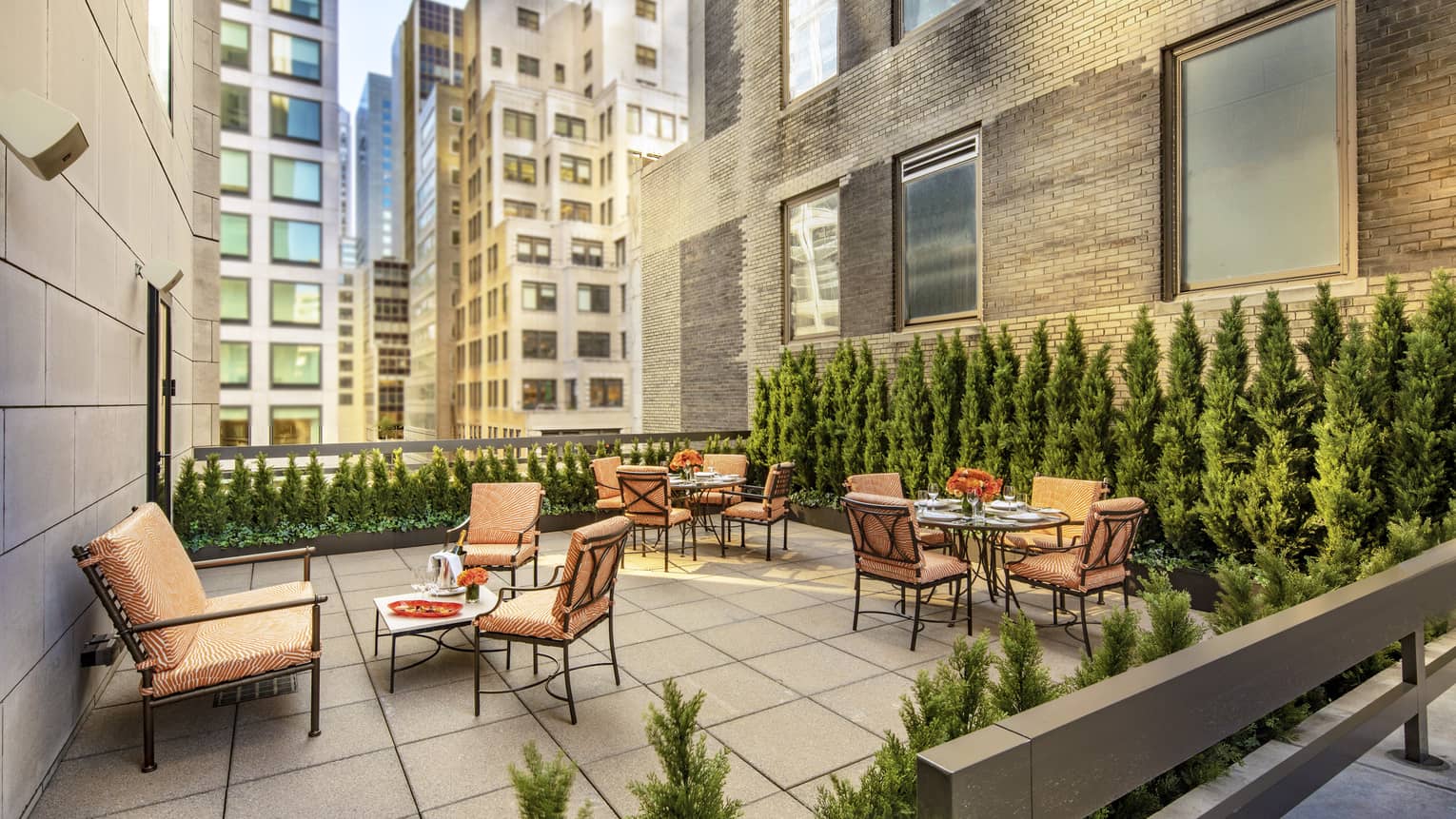 11th Floor Terrace Boardroom surrounded by green topiaries, with iron and glass square tables and orange cushions on chairs at four seasons hotel new york