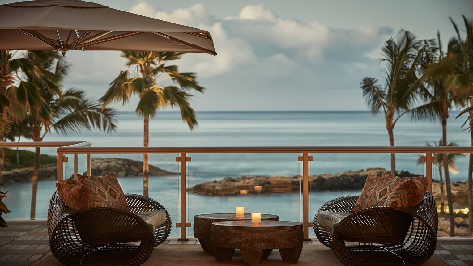 Large rattan chairs with print pillows, table with candles on Hokulea patio at sunset