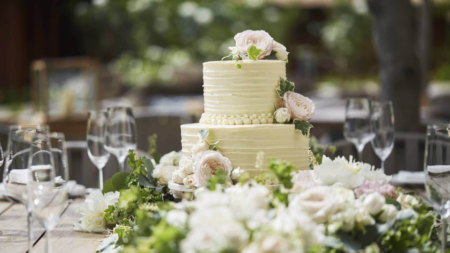 Two-tiered white wedding cake on banquet table with wine glasses, flowers