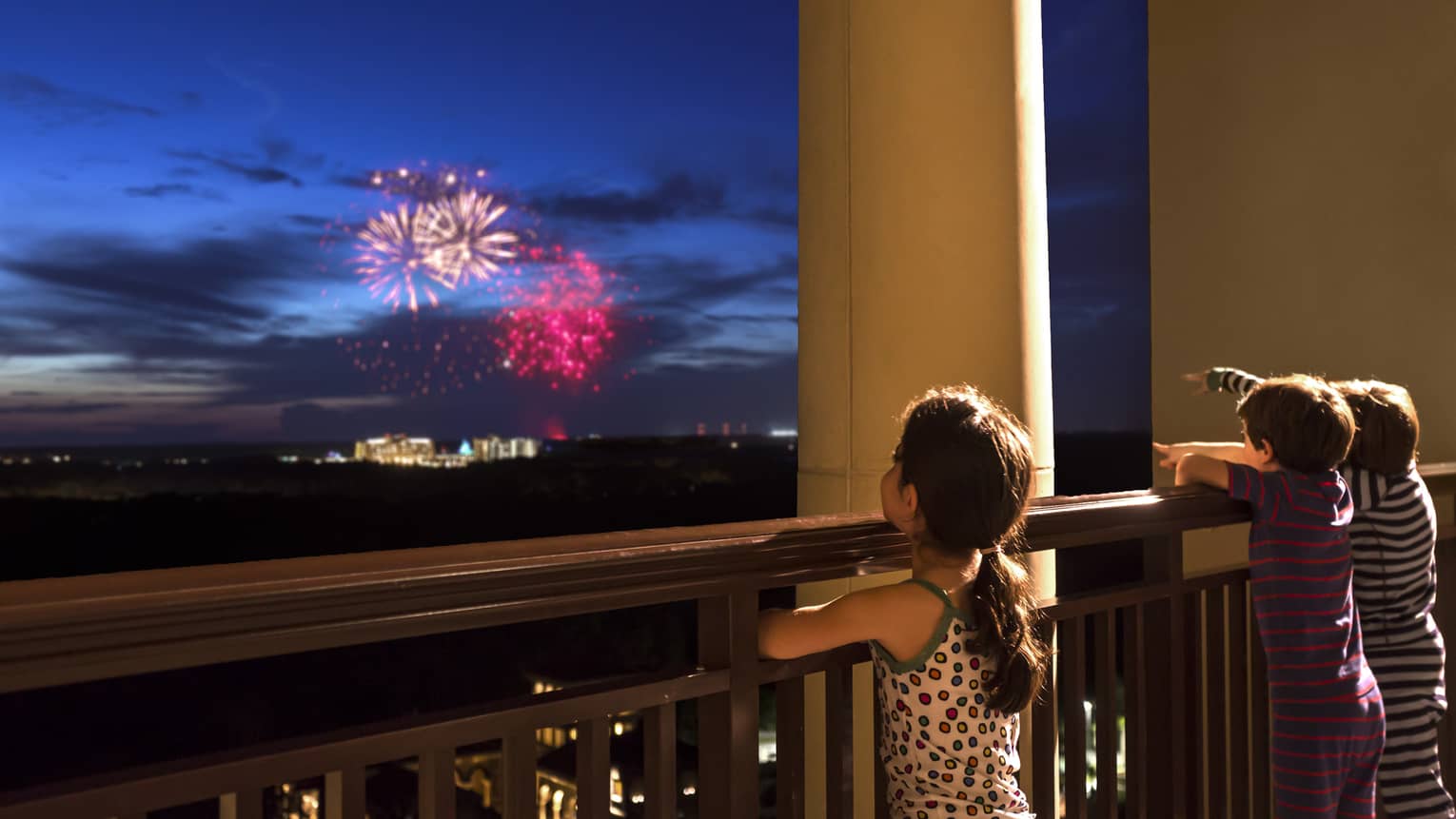 Young girl stands on Four Seasons Hotel balcony, watches colourful fireworks display over Walt Disney World resort