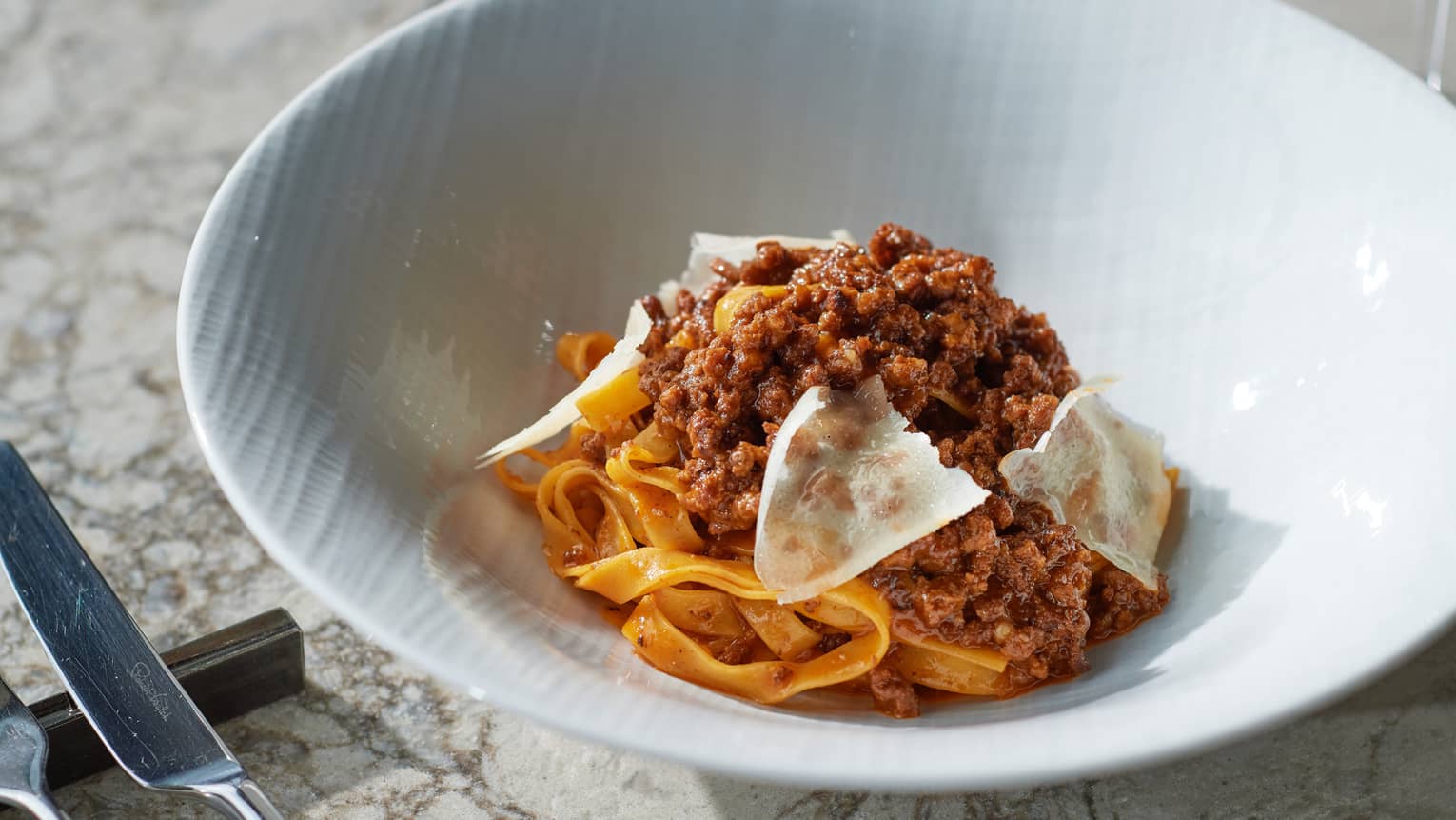 Bolognese Tagliatelle piled high in white bowl, topped with parmesan shavings