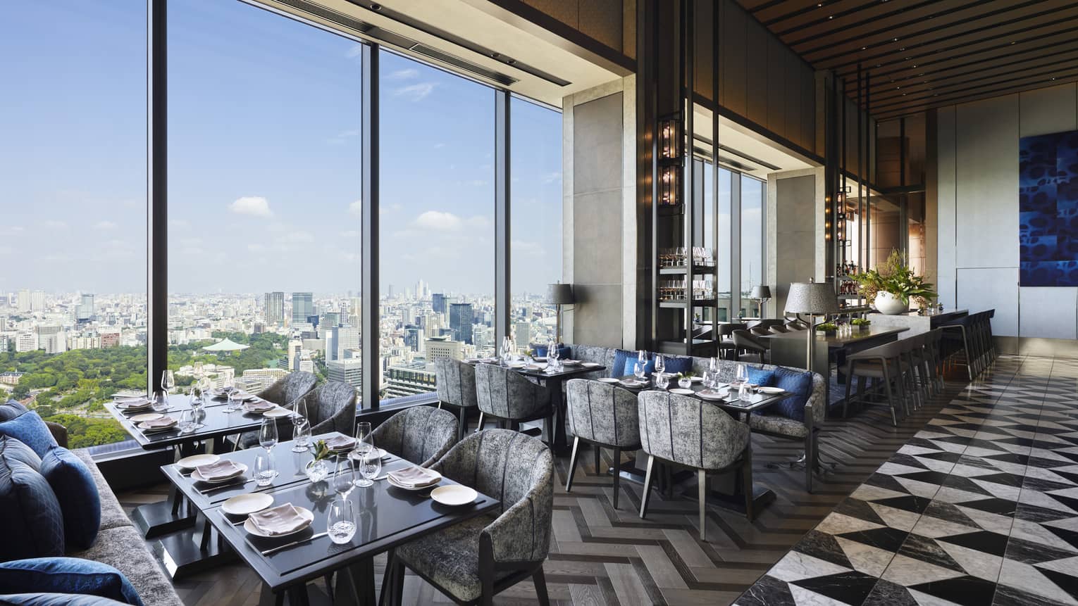 Four tables set for four with floor-to-ceiling windows, view of the city, natural light, grey and black colour scheme