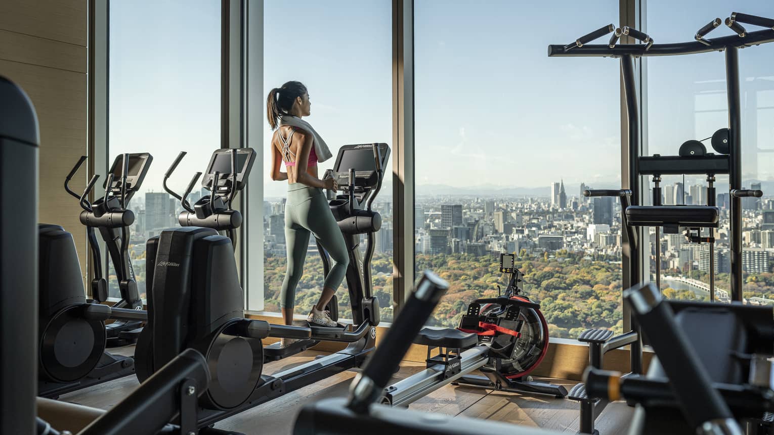 Woman on elliptical gazes out floor-to-ceiling windows of the fitness centre