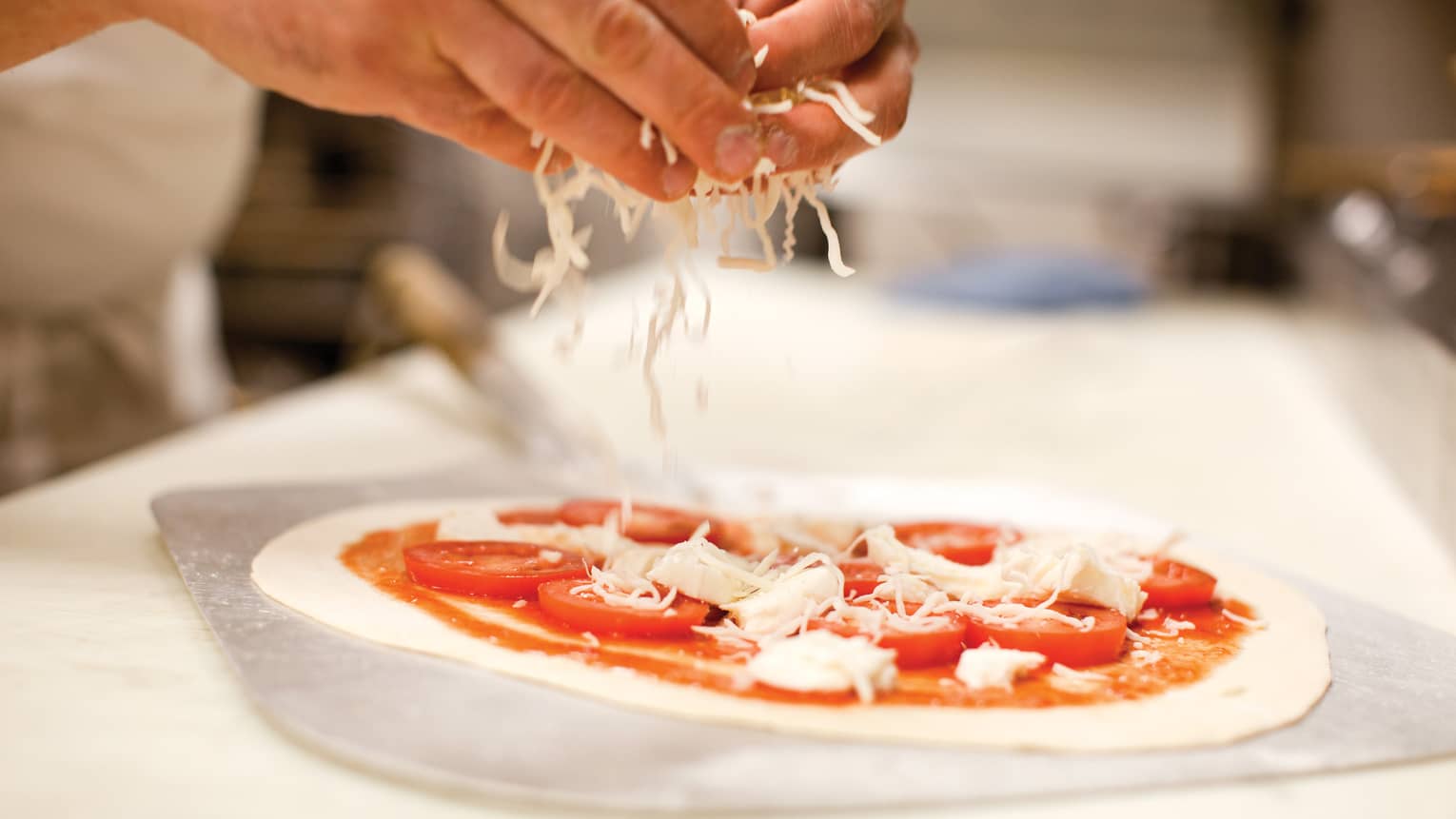 Close-up of hands sprinkling mozzarella cheese on raw personal size pizza