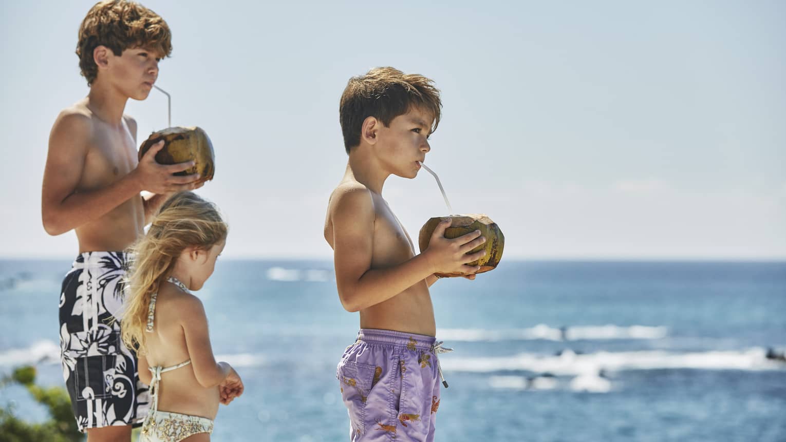 Three guests standing near the ocean and drinking from a coconut.