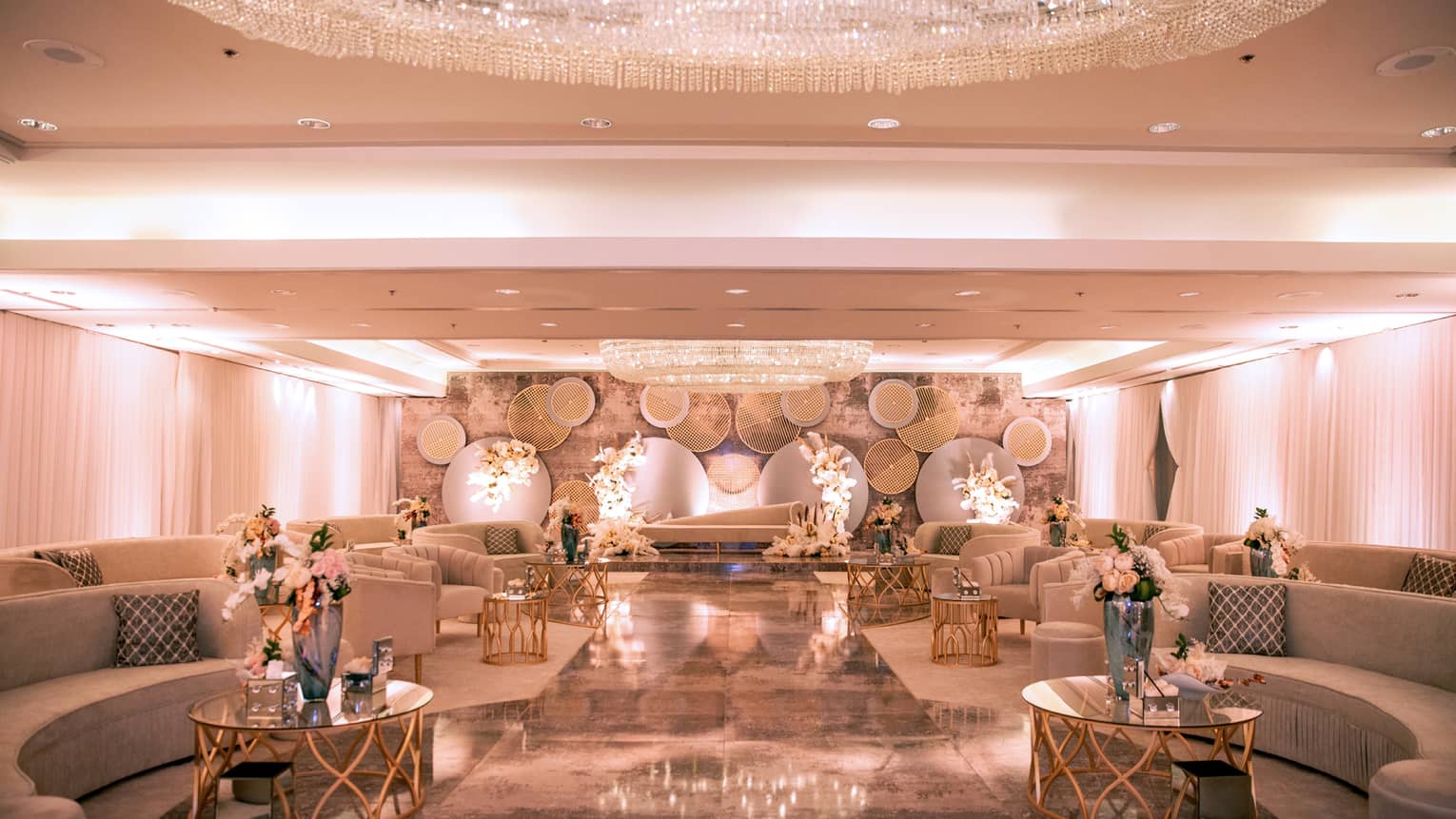 Elegant ballroom with rows of curved sofas, coffee tables and flowers under large dome chandelier