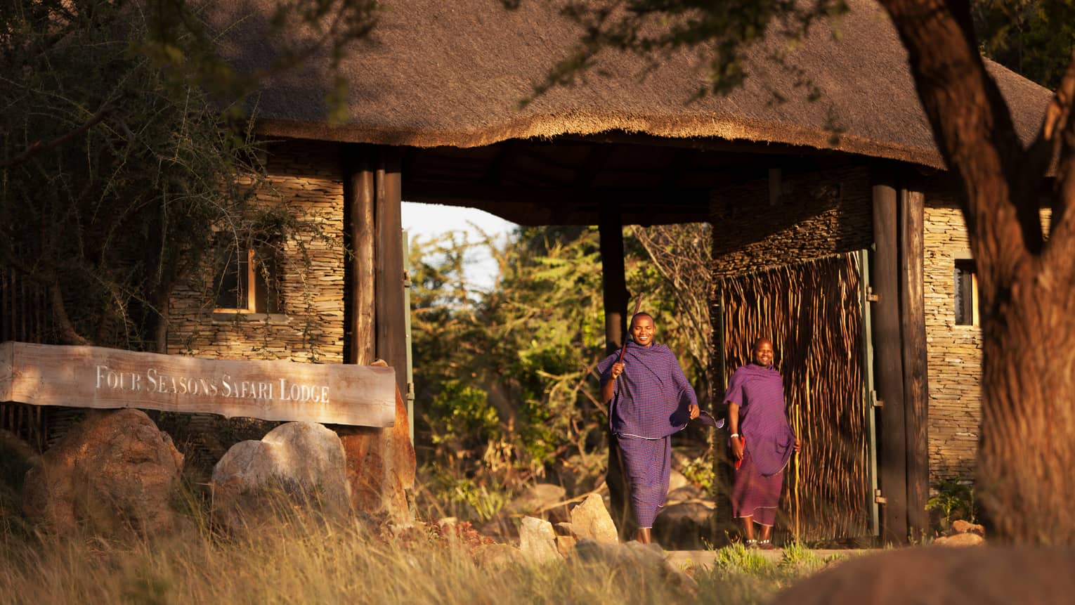 Two people from local Maasai smile, stand by Four Seasons Safari Lodge Serengeti sign