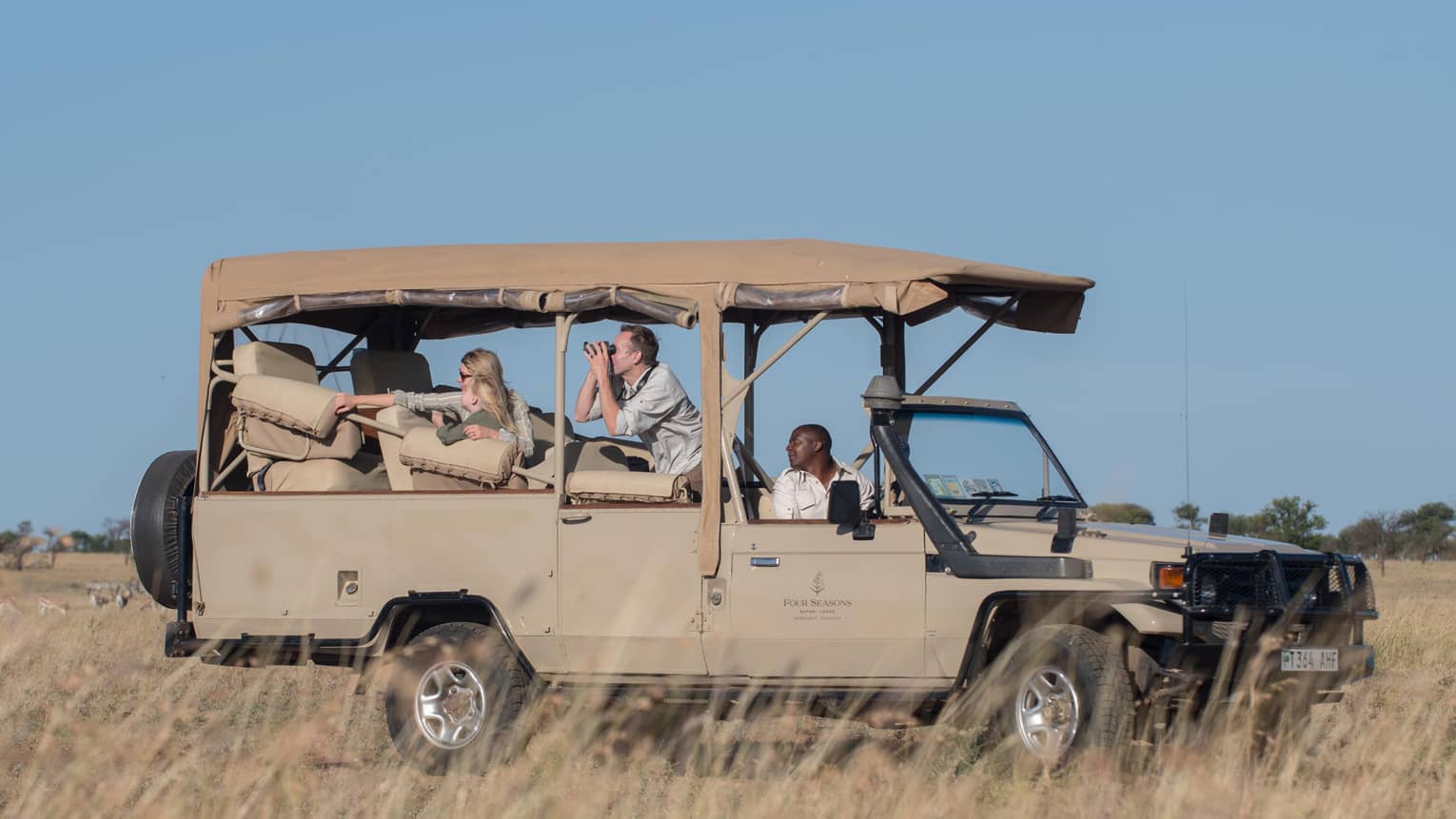 Family looks out over grassy plain from tan safari Jeep