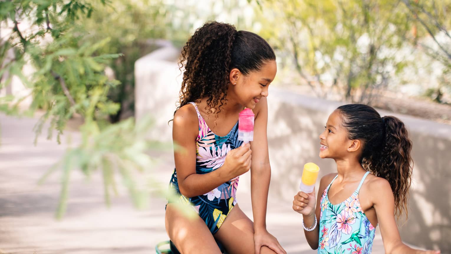 Two young sisters eating ice cream in swimsuits.