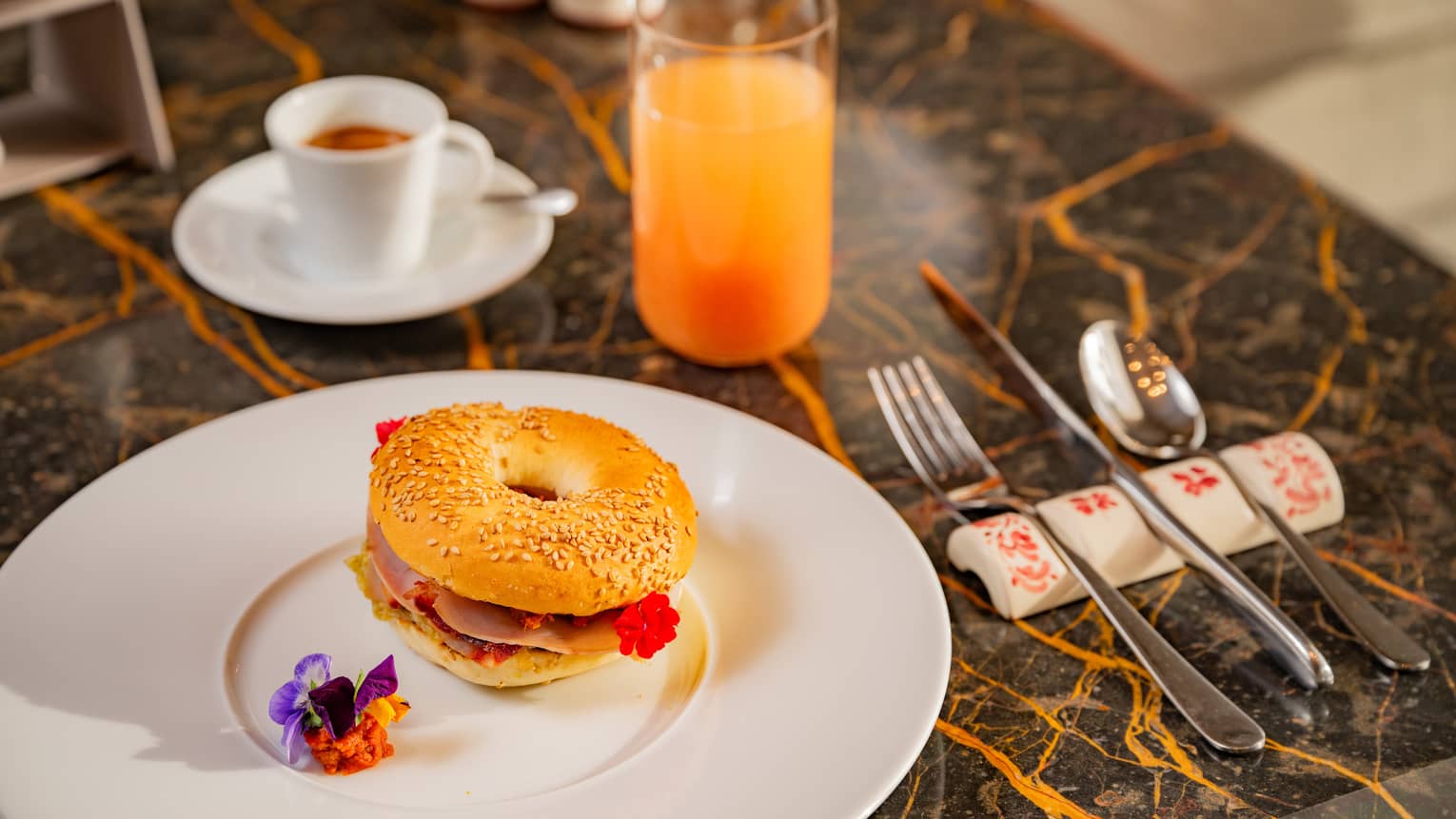 Sicilian bagel with sesame seeds on white plate with flower garnish beside flatware, cup of espresso and glass of juice,Sicilian bagel with sesame seeds on white plate with flower garnish beside flatware, cup of espresso and glass of juice
