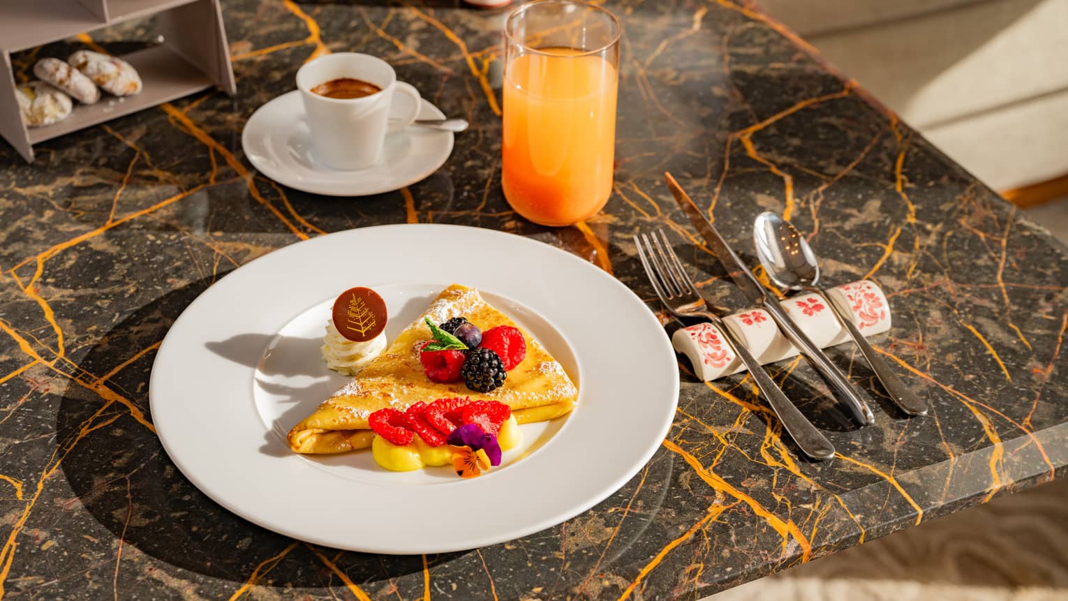 Folded cr�pe topped with mixed berries beside flatware, cup of espresso and glass of juice