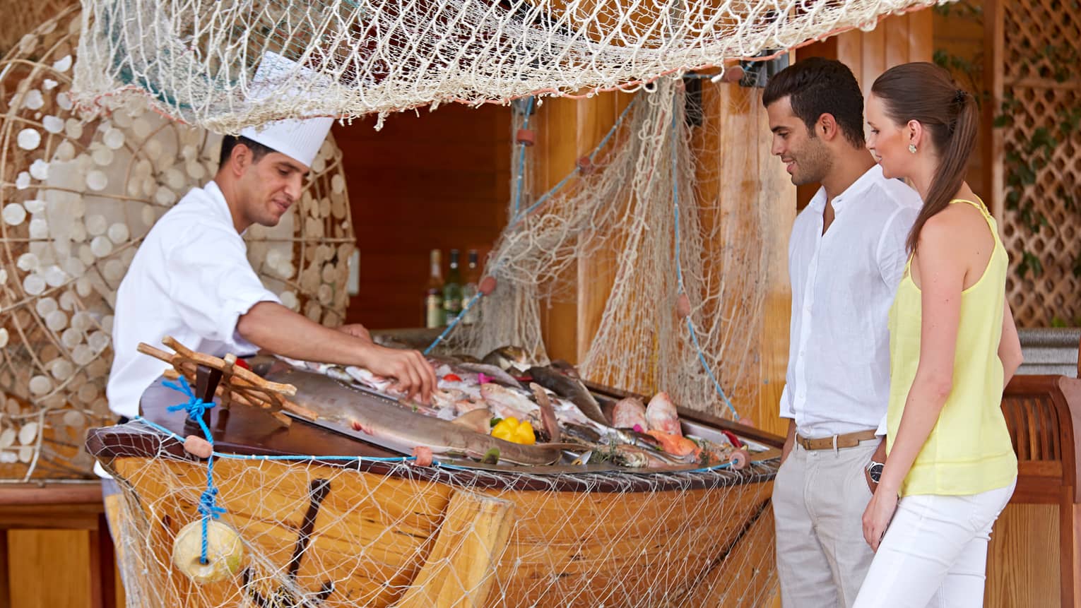 Reef Grill chef in hat displays fresh seafood on ice for couple