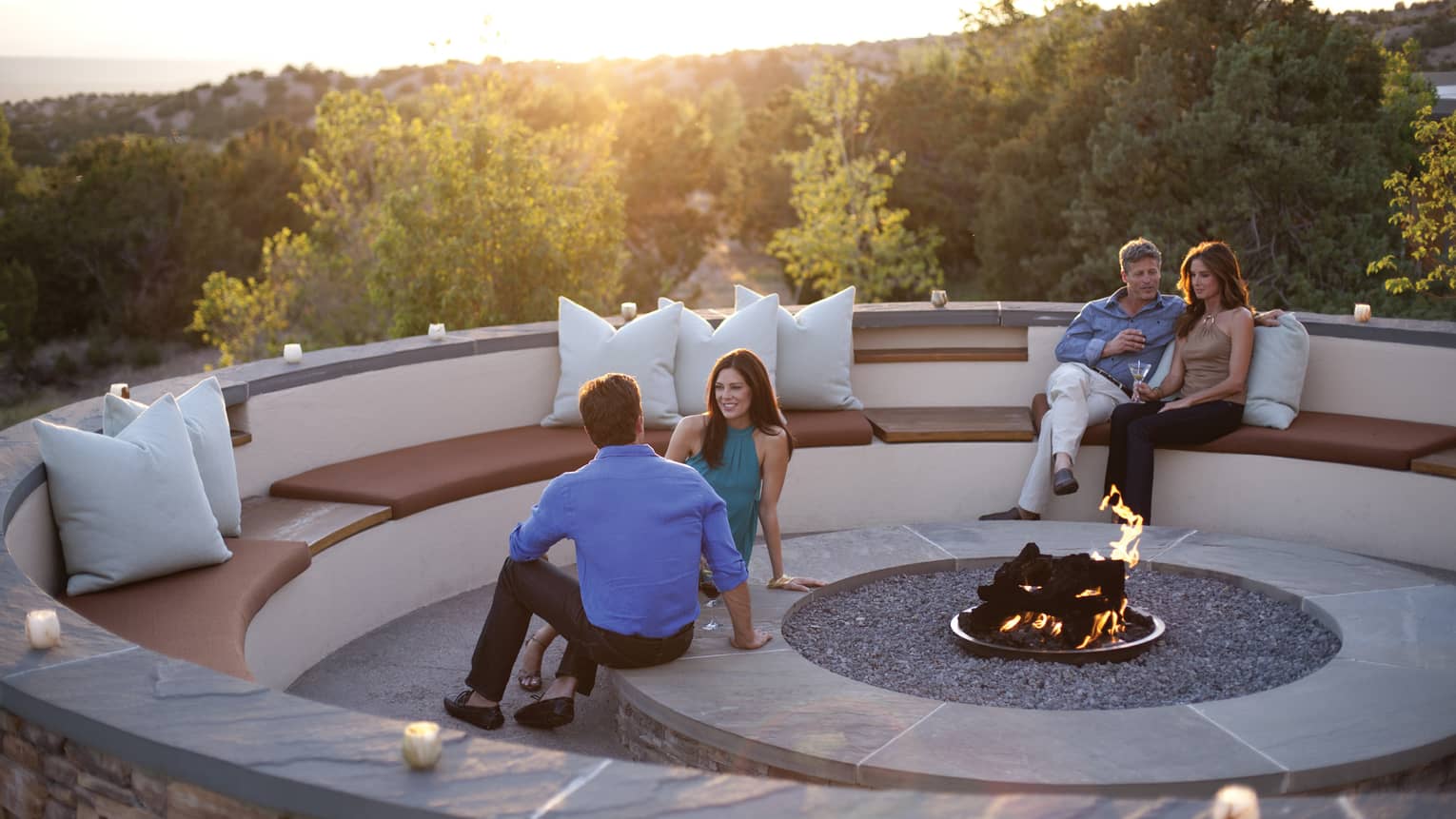 Couples sit within round, stone patio benches, modern outdoor fireplace