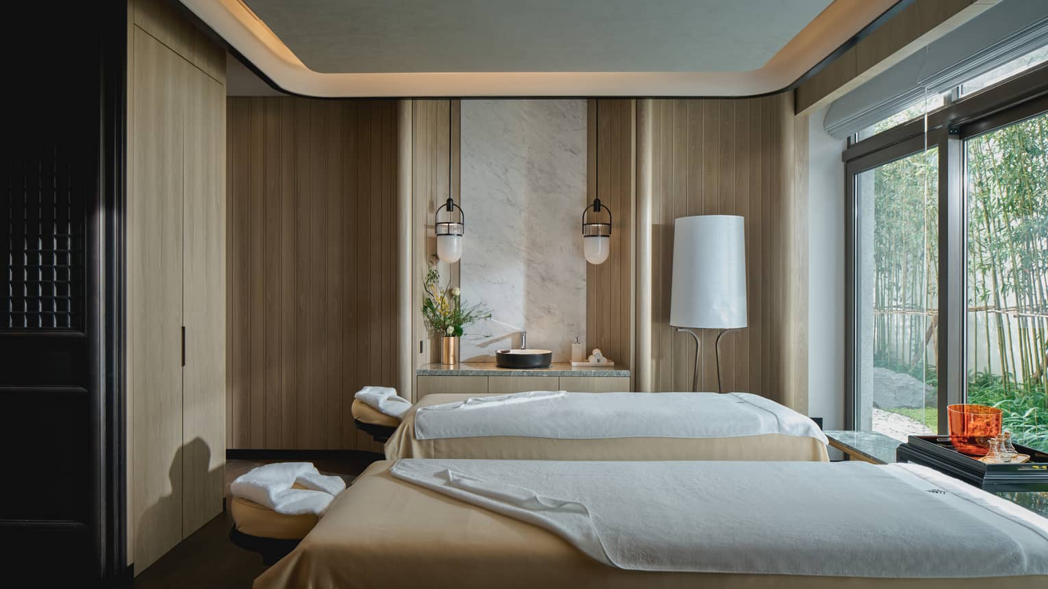 Two spa beds draped with tan and white blankets in front of tall windows