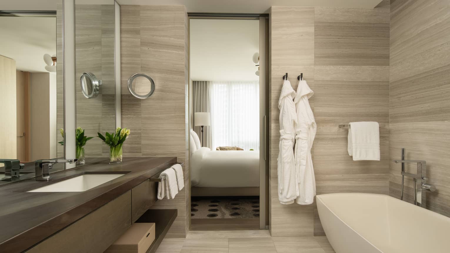 Hotel suite bathroom with long vanity, separate tub and two hanging bathrobes at Four Seasons Hotel Toronto