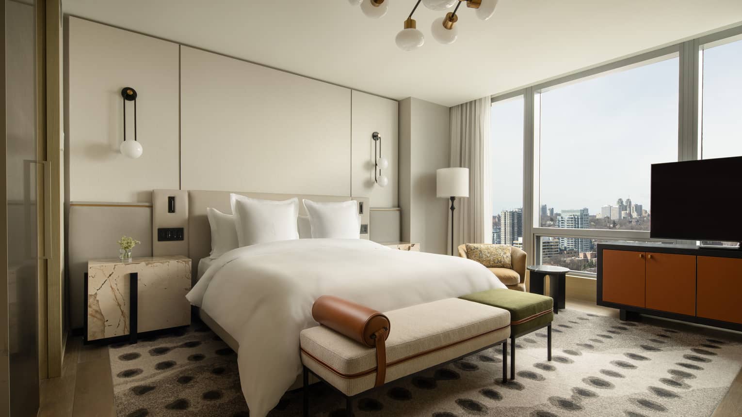 Hotel suite bedroom with king bed, stylish lighting fixture and wall of windows at Four Seasons Hotel Toronto