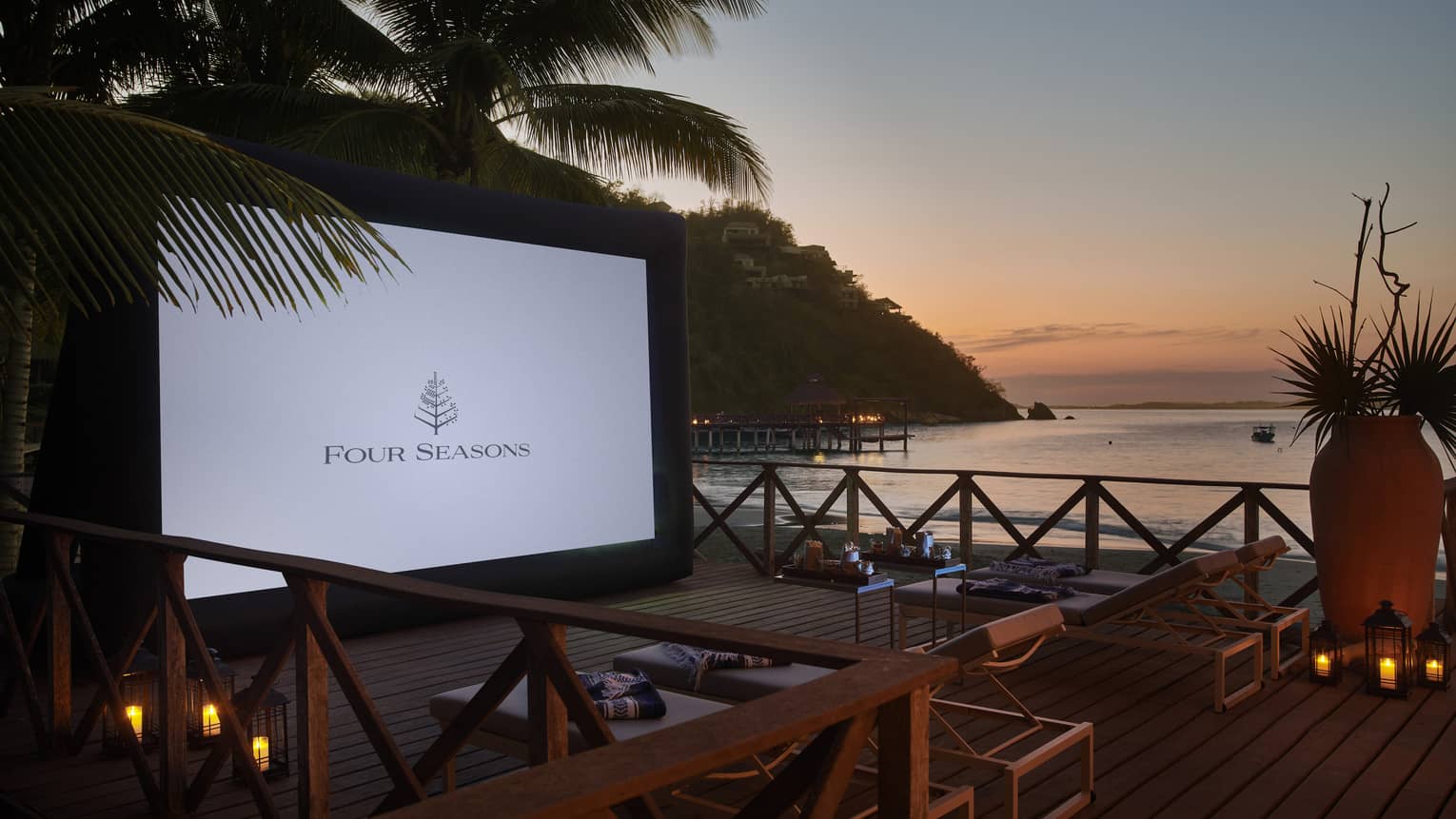 A large outdoor screen near palm trees and the ocean.
