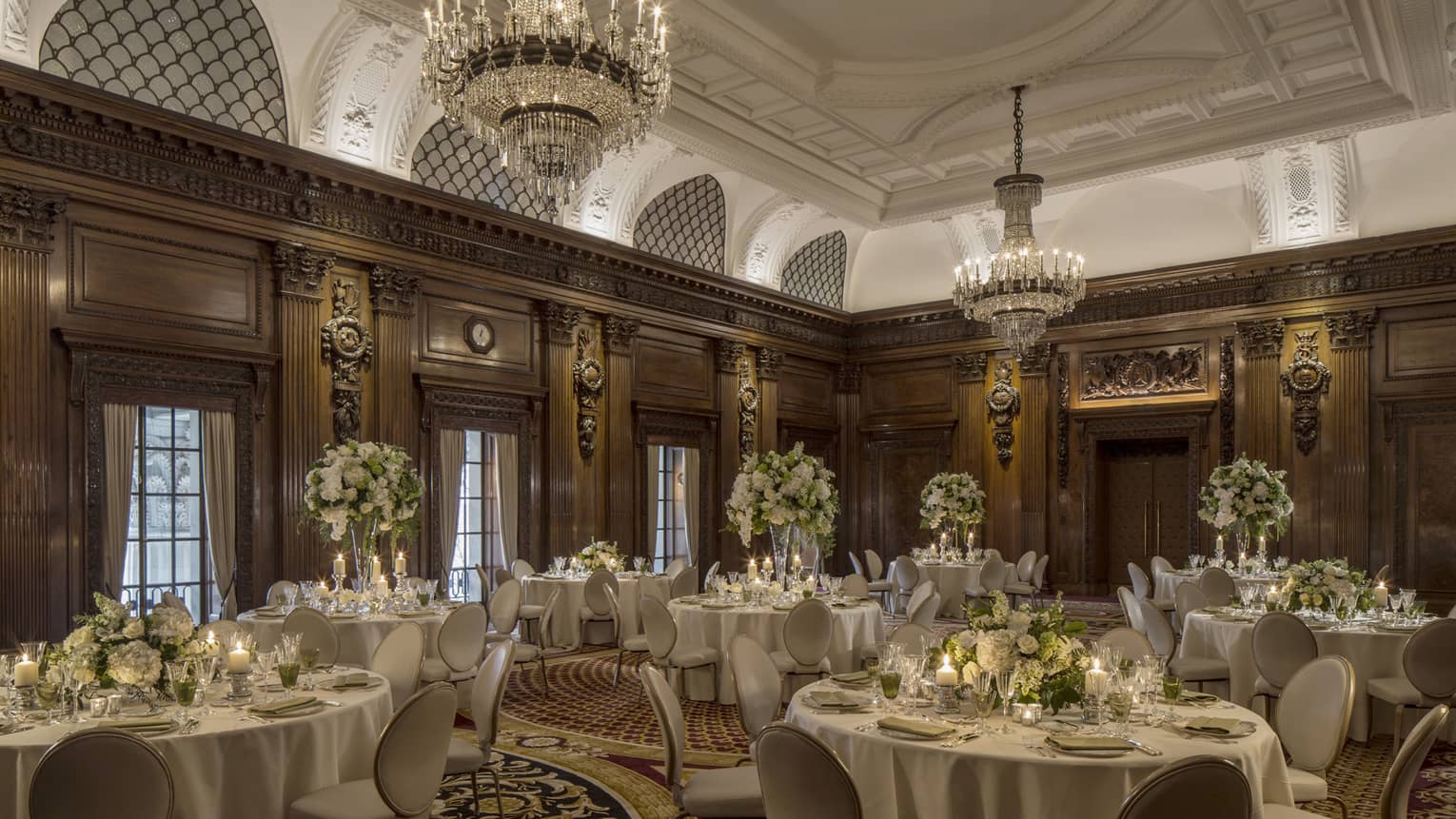 Elegant ballroom with decorative wood walls, crystal chandeliers over round banquet dining tables