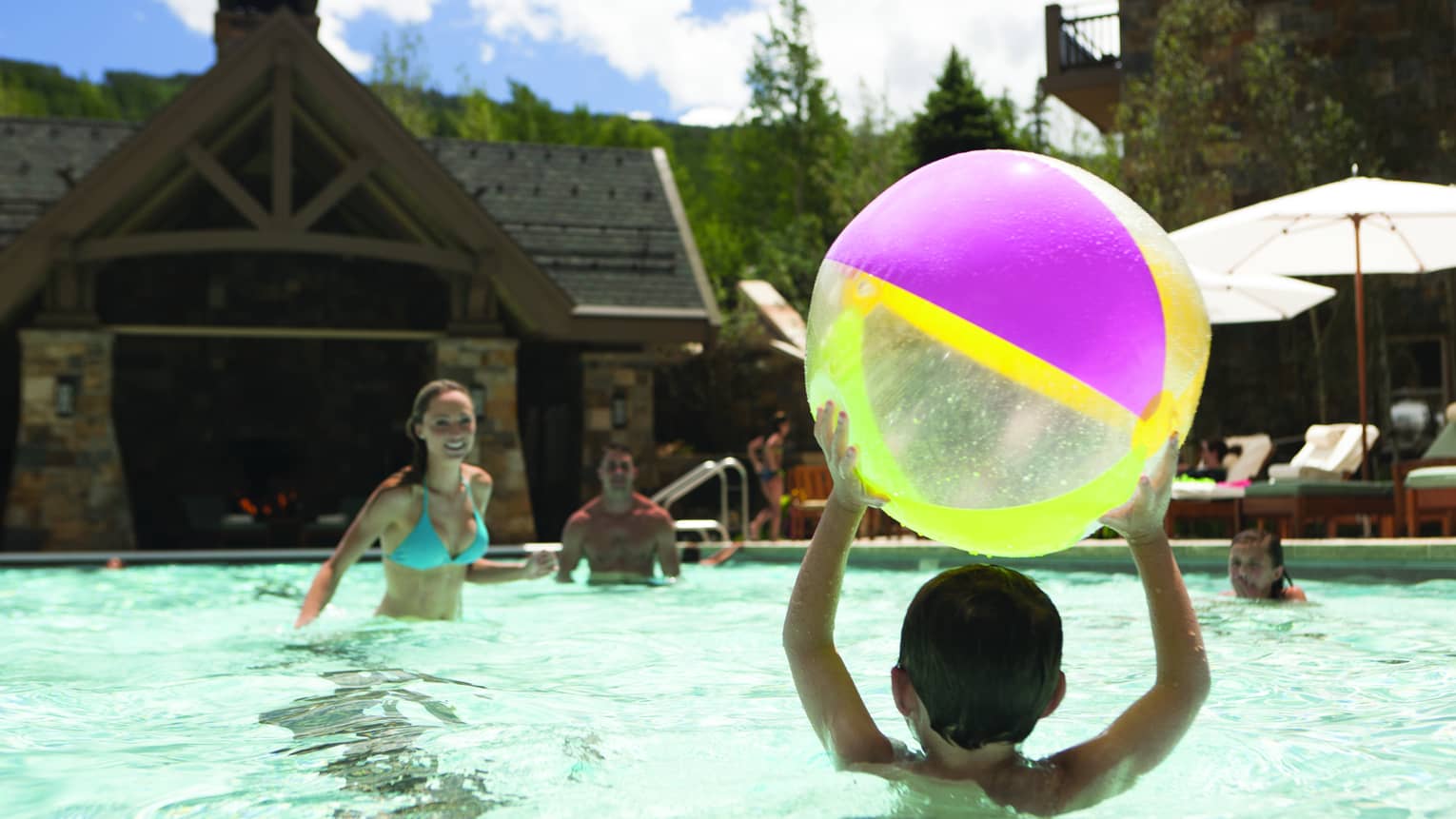 A group of children and young people playing with a beach ball in an outdoor pool.