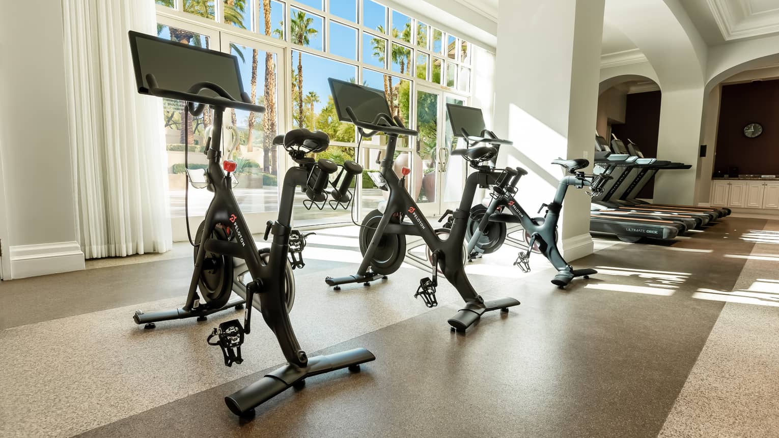 Three Peloton bikes near large windows.