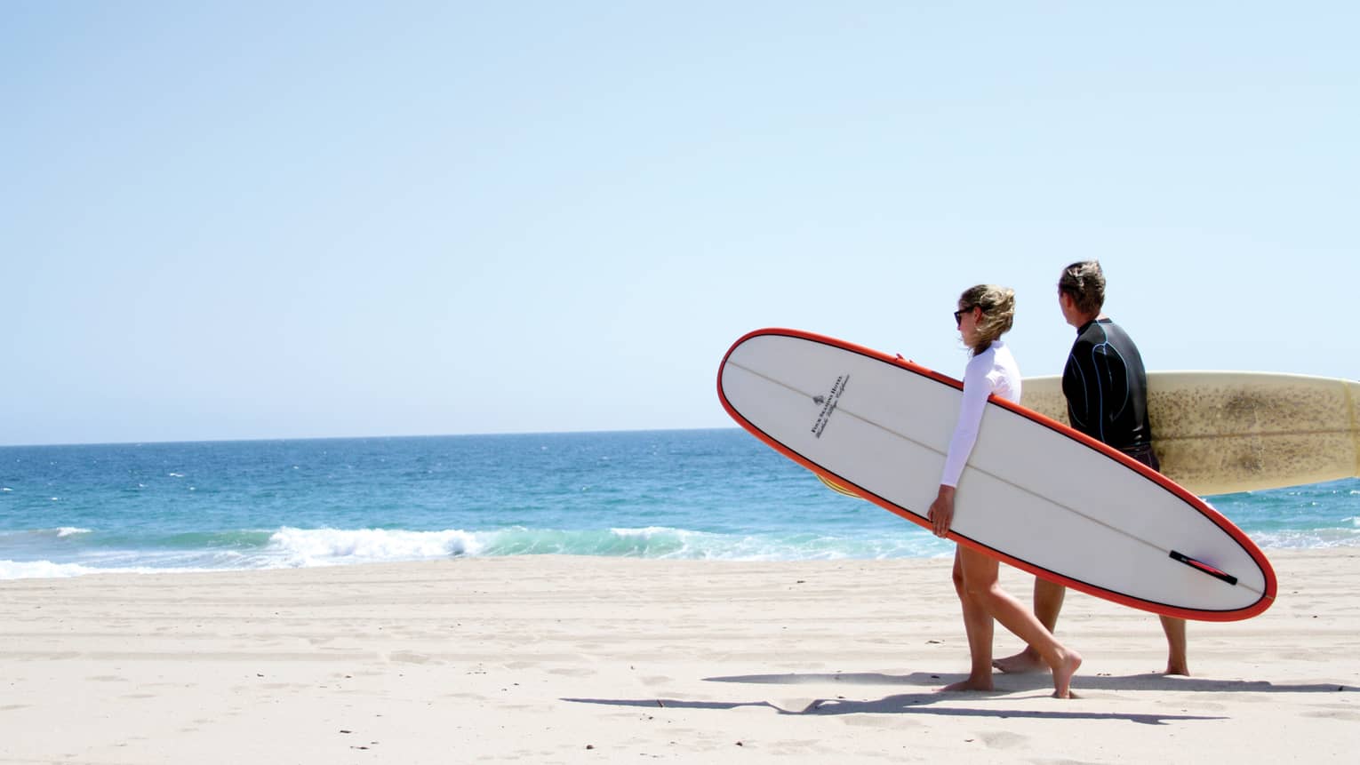 A couple on the beach holding surfboards under their arms.