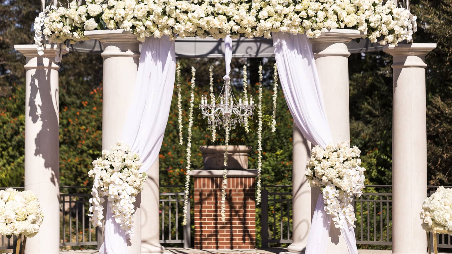 Outdoor wedding ceremony altar with white drapes, flowers