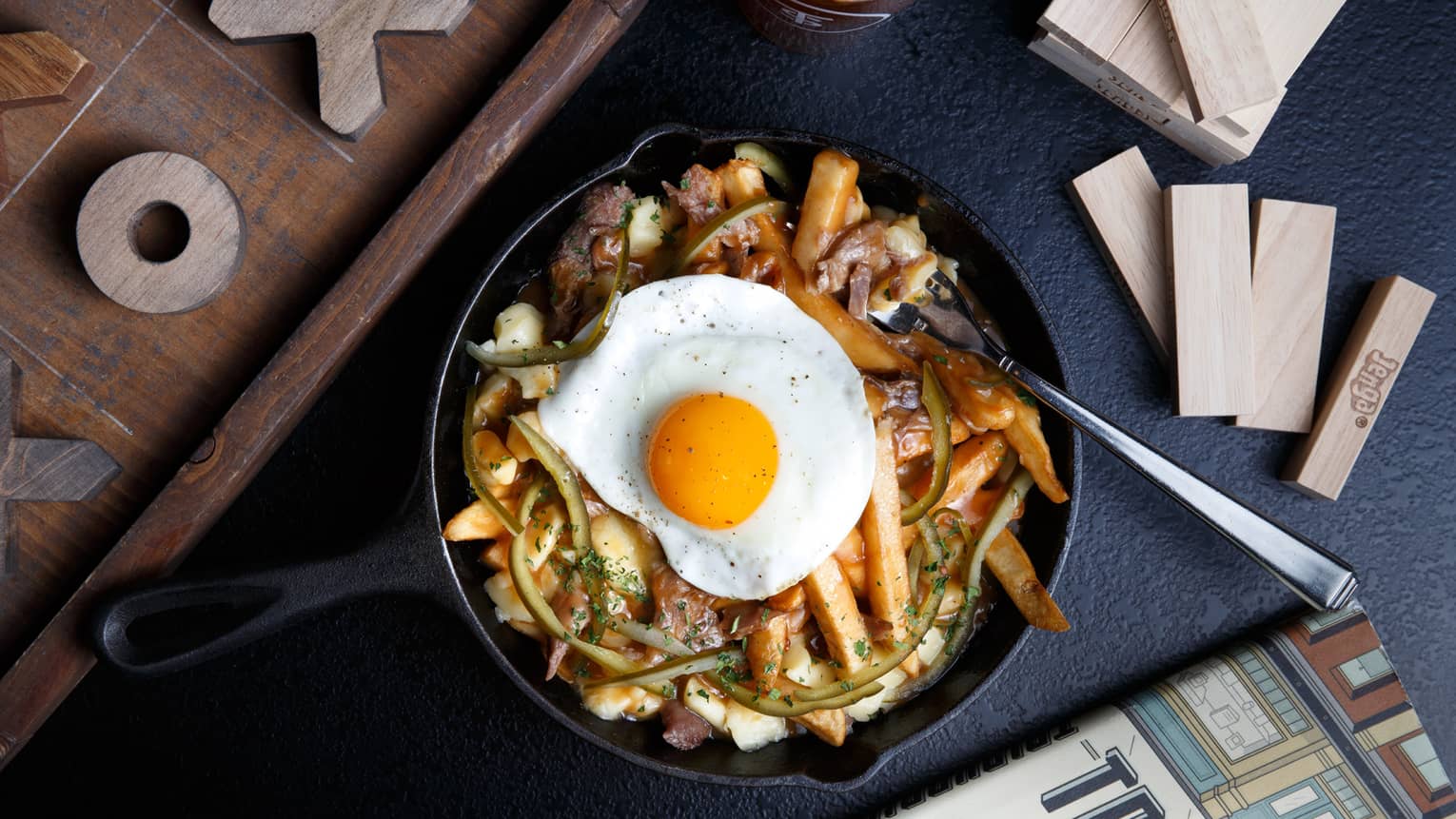 A skillet filled with fries, various spices and a fried egg.