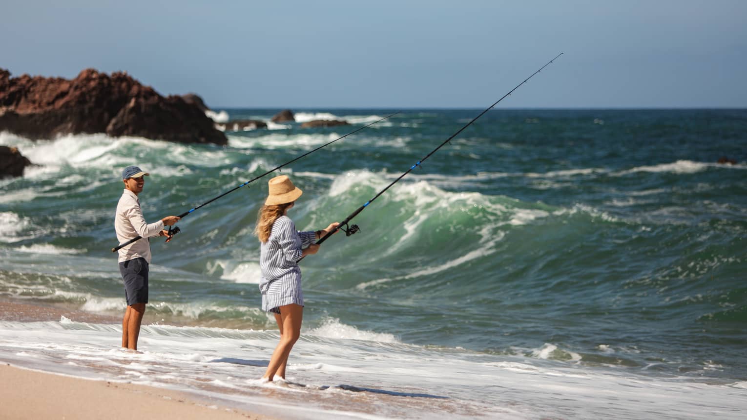 Two people fishing on a beach shore.