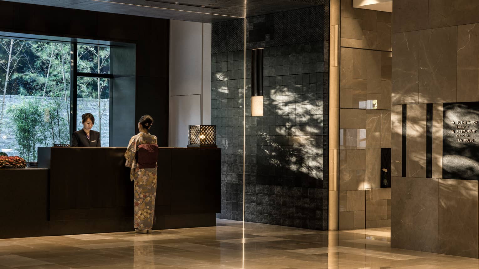 Woman in silk kimono stands at reception desk in marble Four Seasons Hotel Kyoto lobby