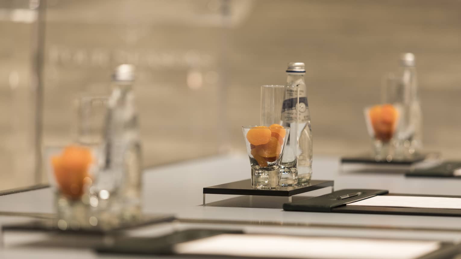 Close-up of meeting table place setting with agenda, dried apricots in glass, bottle of sparkling water