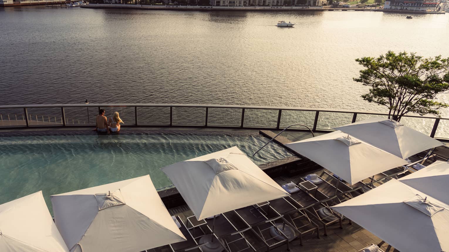 Two people sitting on the edge of a pool overlooking the harbour.