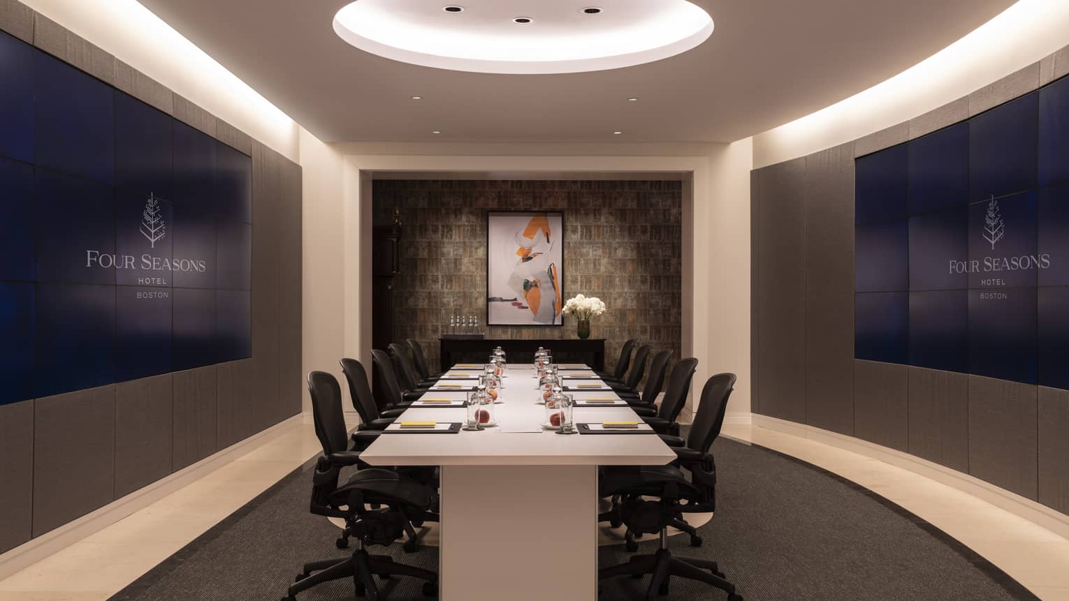 A meeting room with a large white boardroom table surrounded by black chairs with wheels.