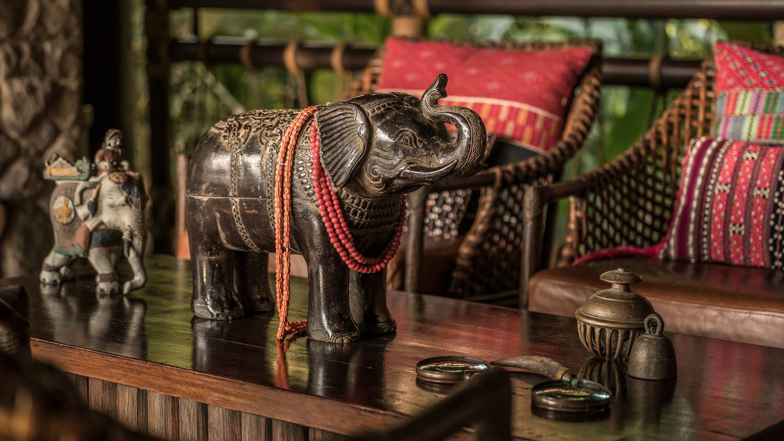 Elephant statue on wood table in front of bamboo sofa with red cushions
