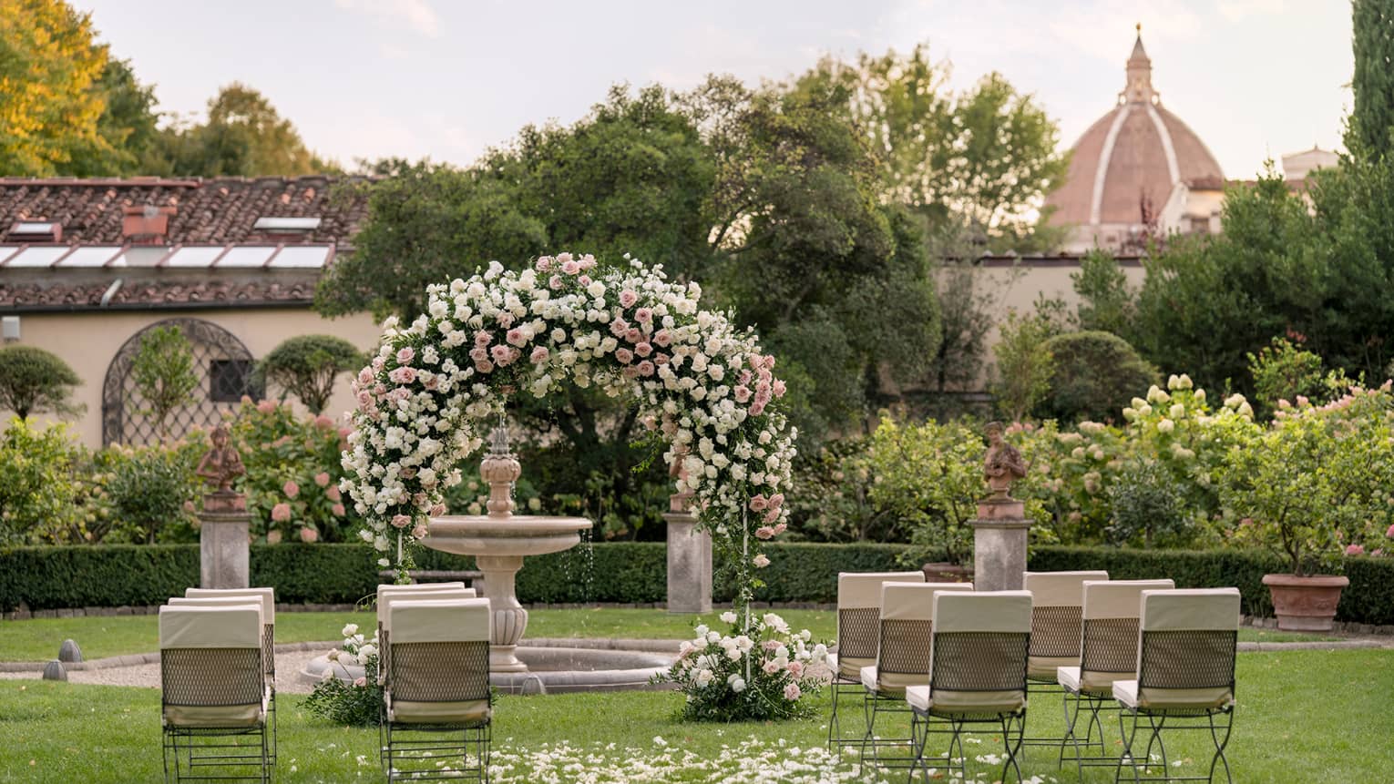 Garden wedding setup with floral archway and view of Duomo in backdrop