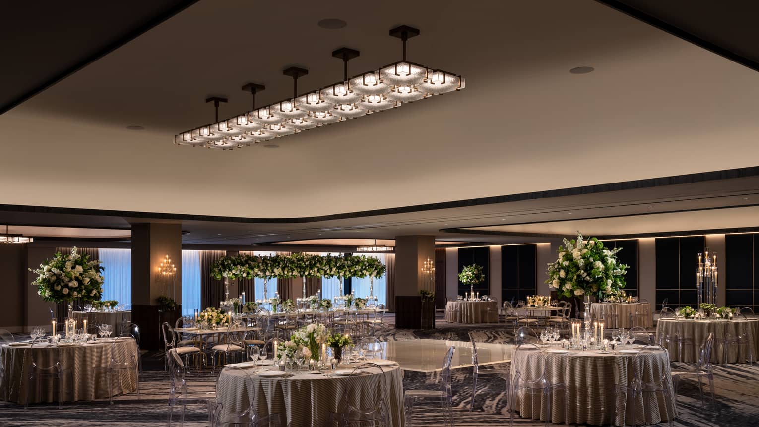 A ballroom with round tables and grey table clothes with flowers and plants as centerpieces on the tables.