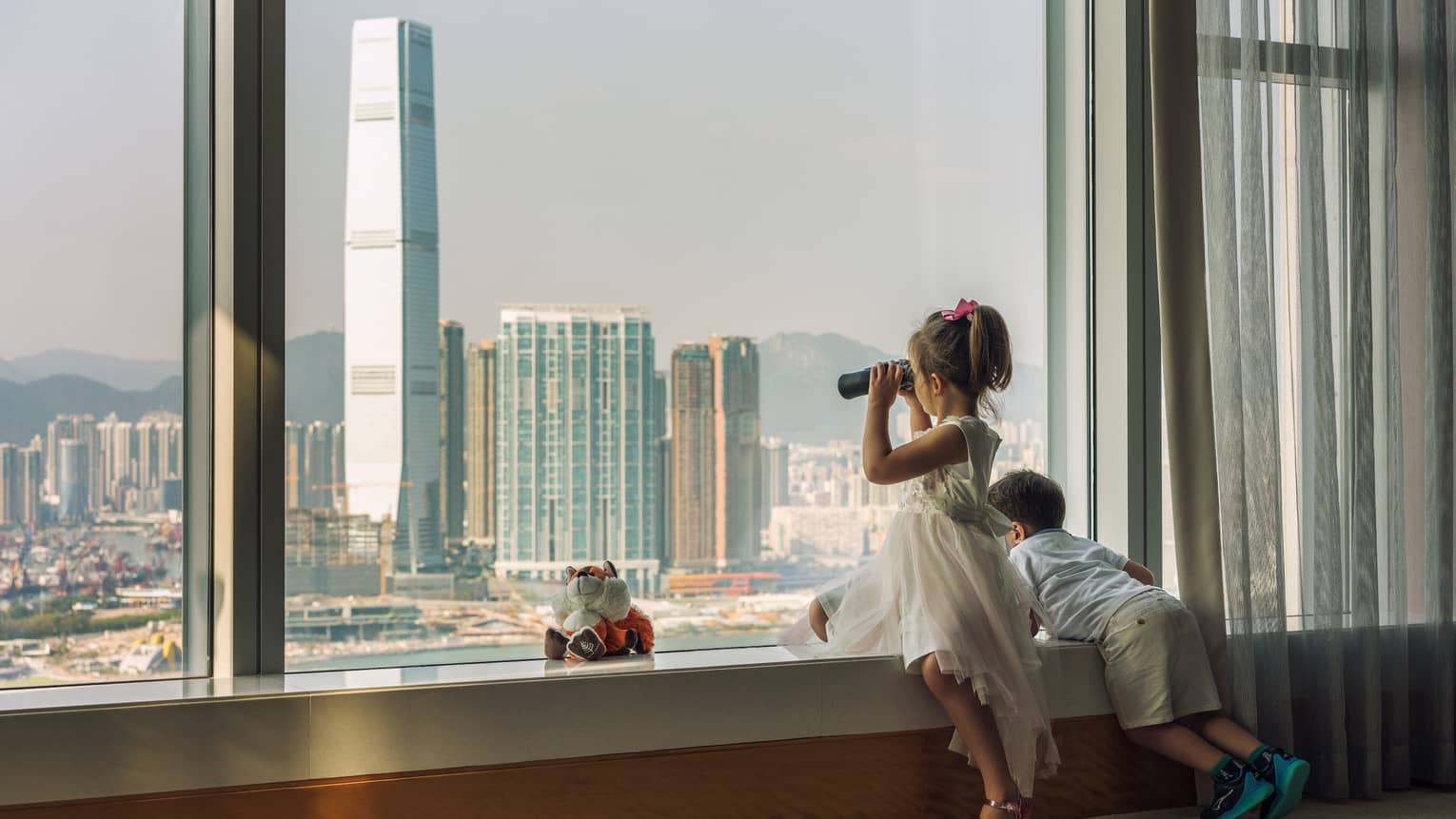 Young boy and girl looking out hotel window to Hong Kong cityscape