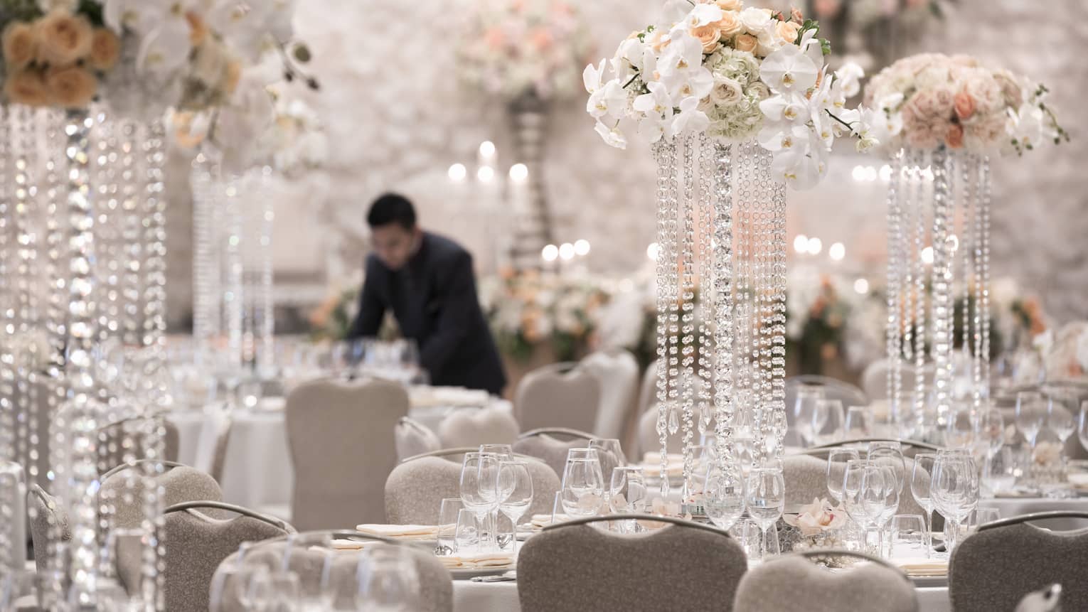 Hotel staff sets elegant ballroom banquet tables with white flowers, crystal ware 