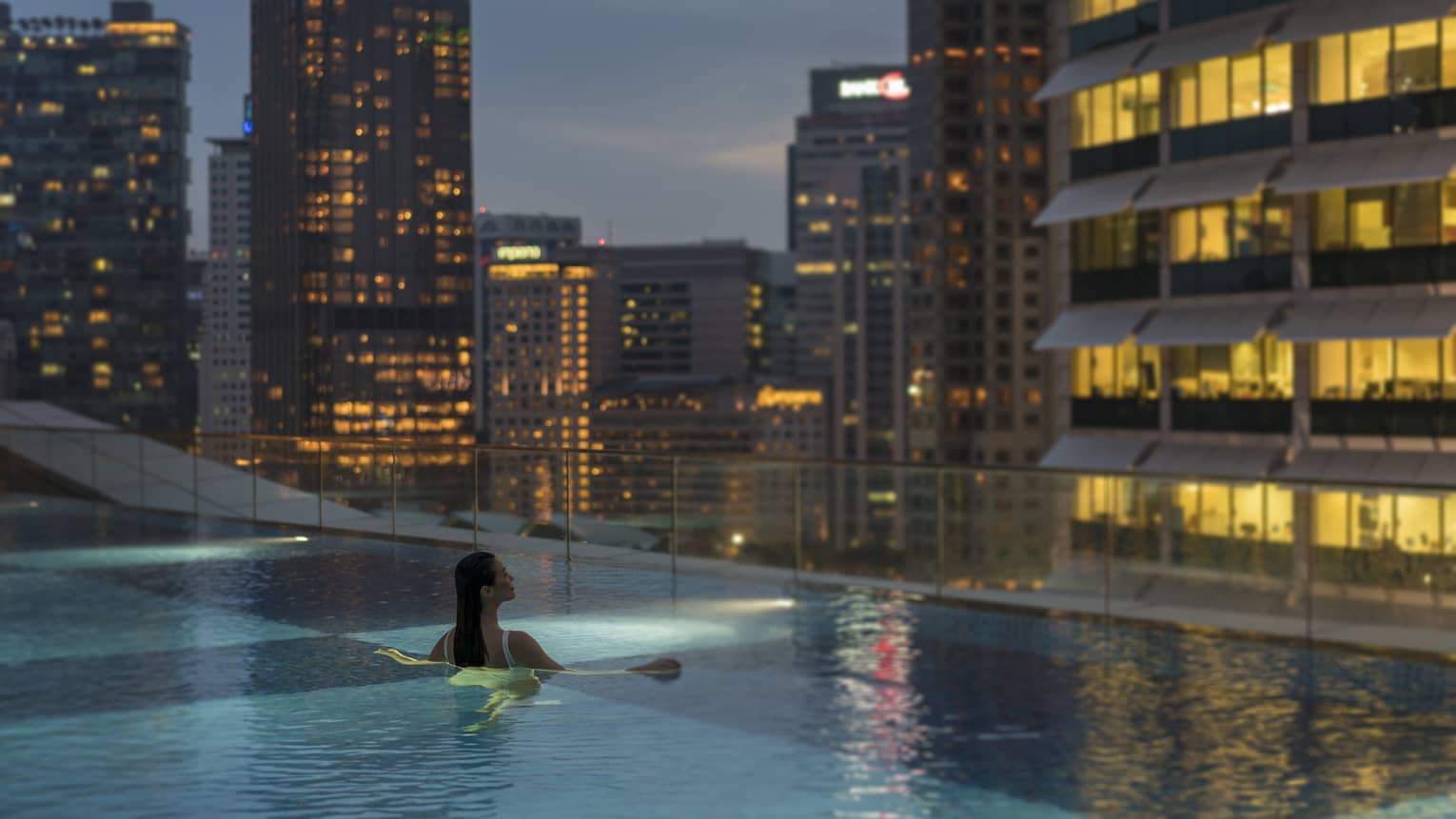 A woman swims in an infinity pool with a view of the city skyline
