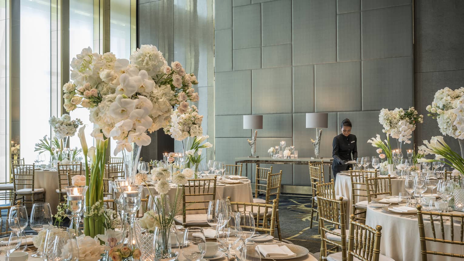 Hotel staff sets table in Western Banquet room with round tables, white flowers 