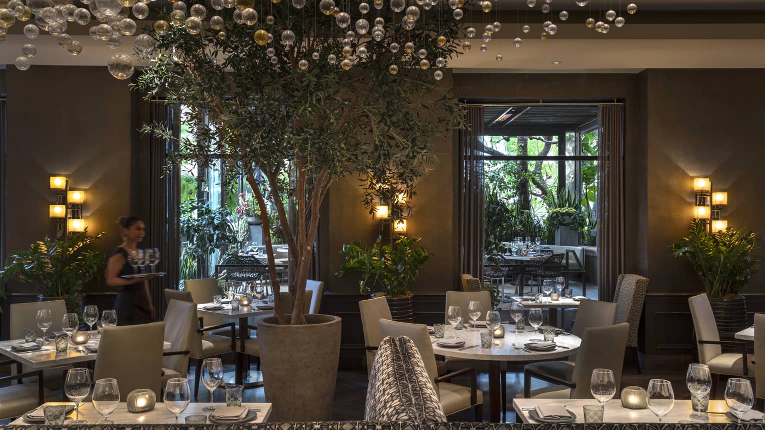 The interior of a dimly lit restaurant with white tables and grey chairs and bubble glass hanging like a chandelier.