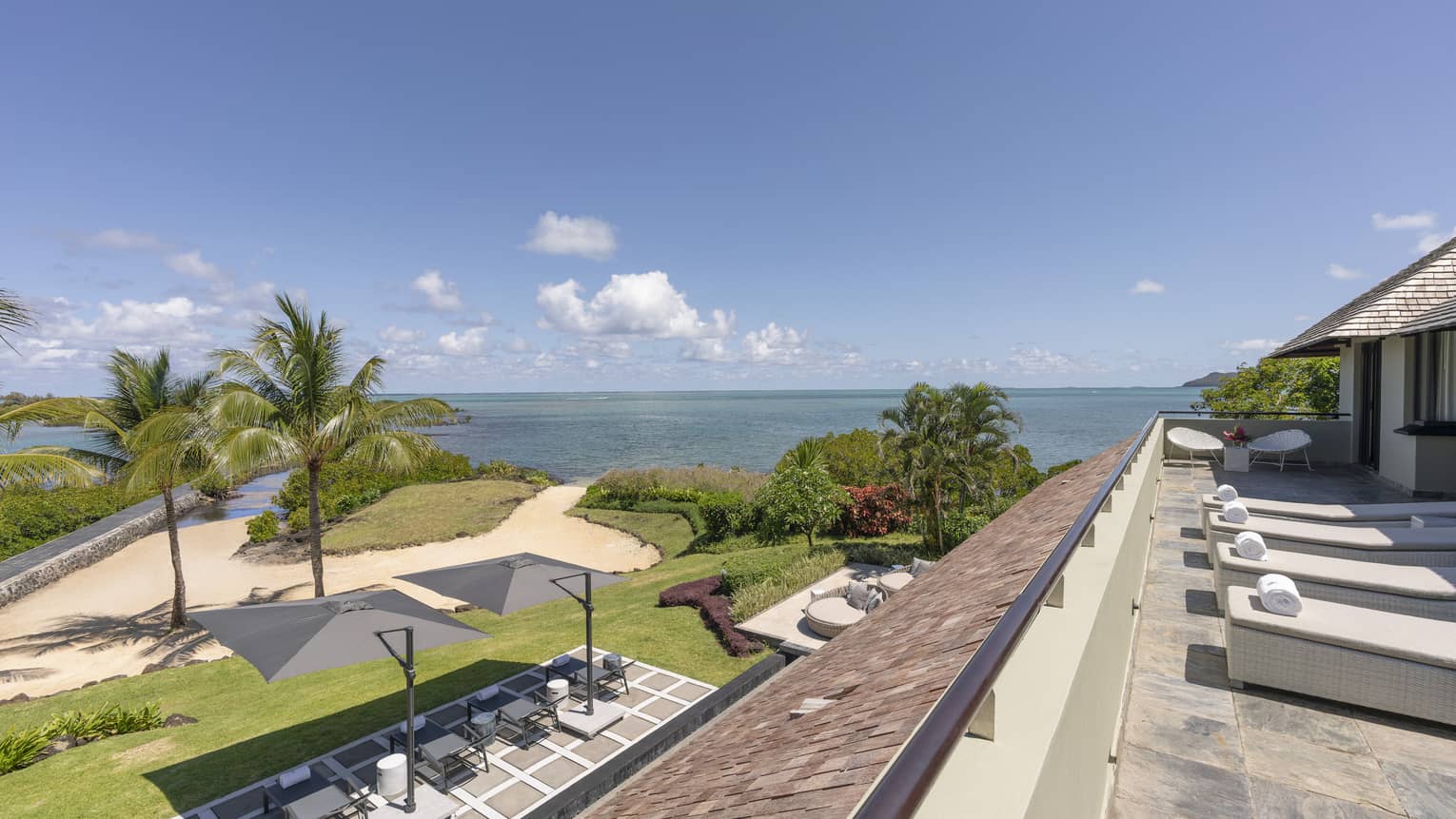 Ocean-view terrace with lounge chairs overlooking tropical lawn