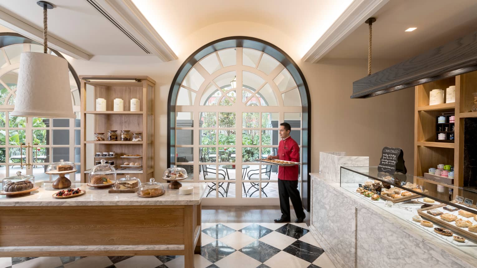 Sunny Pan Dulce cafe, man carries pastry tray across black-and-white tile floor to bakery counter