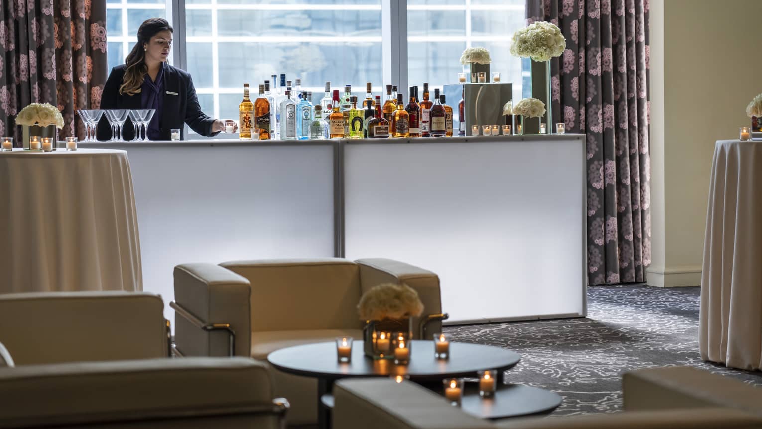 Bartender stands at liquor bottle-lined bar in front of window near seating area