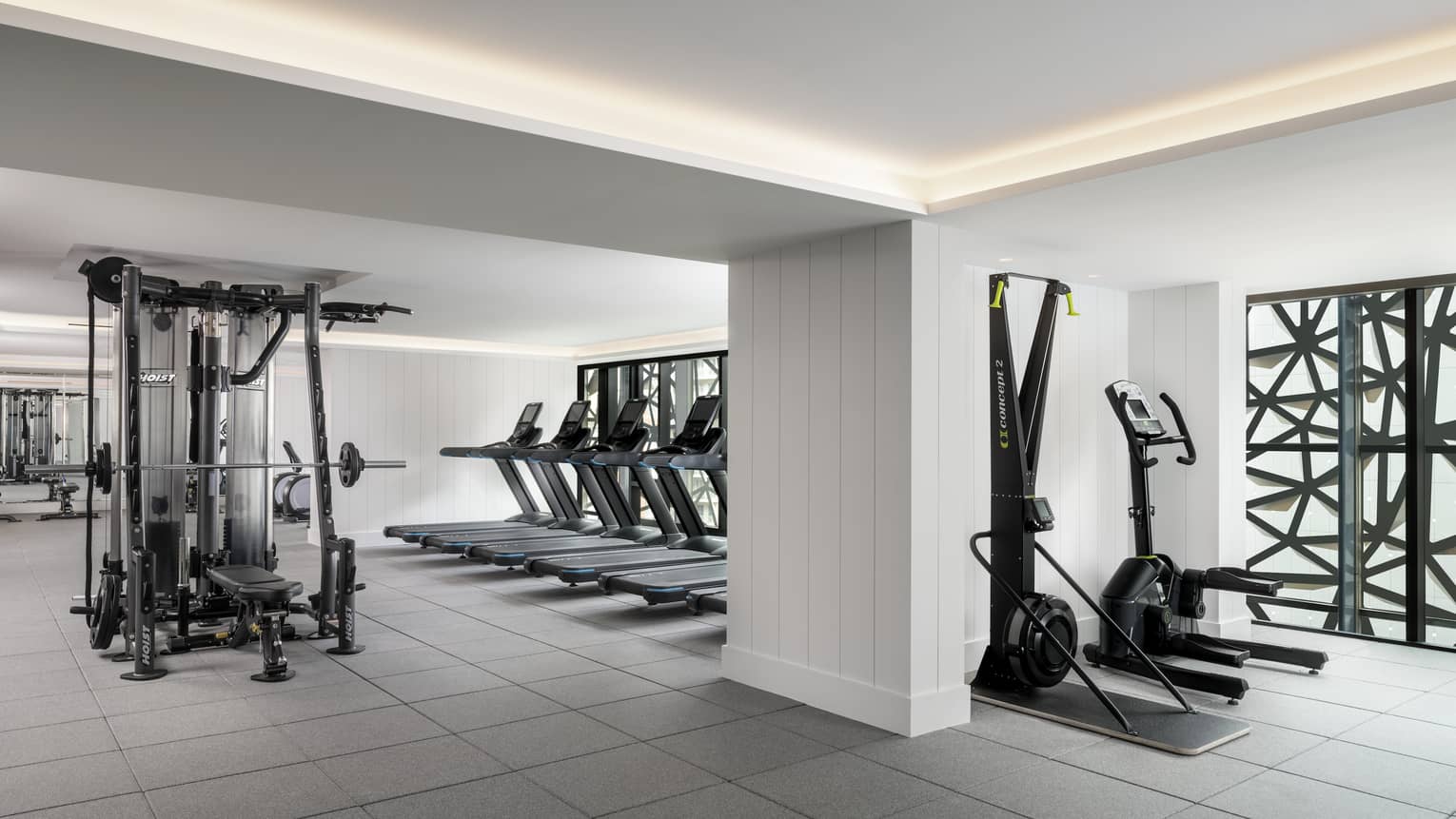 A large fitness space featuring a weights machine and several ellipticals. 