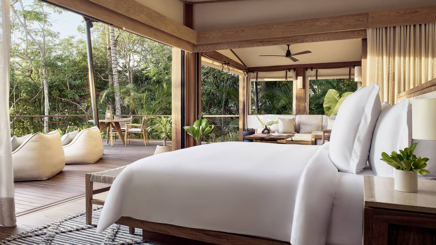 Bedroom of a luxury tent, open to a deck and surrounded by tropical forest