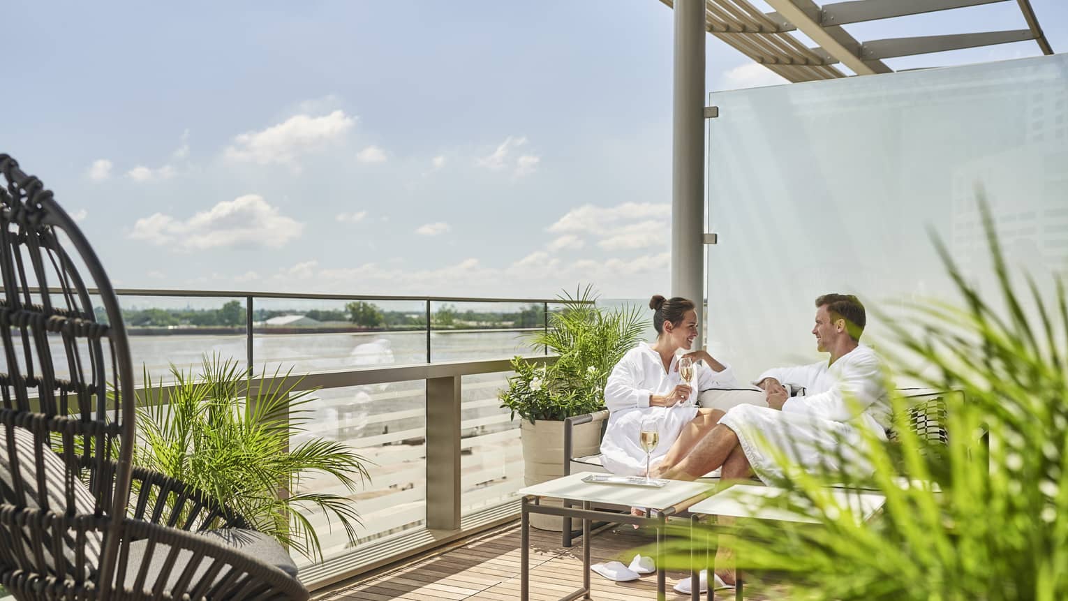 A man and woman in spa robes sitting on a patio with plants.